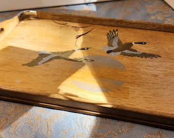 May include: A wooden serving tray with silver trim features a painted design of two geese flying over a moon. The tray has two handles on the sides.