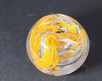 May include: A clear glass paperweight with yellow, white, and blue swirls inside.
