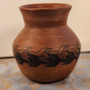 May include: A small, terracotta-colored pottery vase with a black design of stylized birds in flight around the middle.