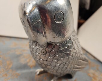 May include: A silver metal bird figurine with a textured surface. The bird has a round head with a small eye and a detailed beak.