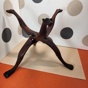 May include: A dark brown wooden sculpture of an animal with outstretched arms and legs. The sculpture has a bear-like head and is made of interlocking pieces of wood. The sculpture is on a tan surface with an orange background.