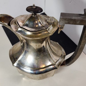 May include: A silver teapot with a wooden handle and a black knob on the lid. The teapot has a decorative, faceted design.