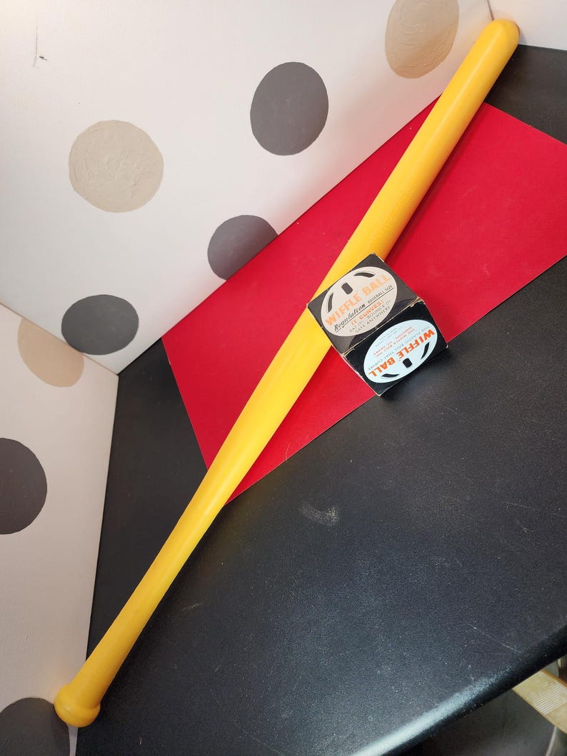 May include: A yellow plastic wiffle ball bat with a black and white box of wiffle balls. The box says "Wiffle Ball" and "Regulation Size".