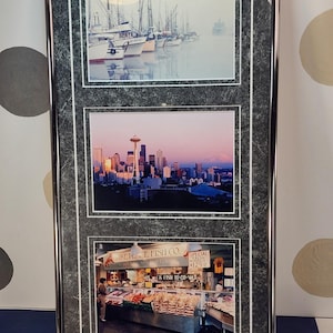 May include: Framed artwork featuring three distinct images. The top image shows boats in a harbor, the middle image depicts a city skyline with a tower, and the bottom image showcases a fish market with text that reads "Pike Place Fish Co."