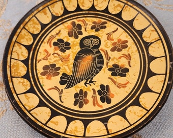 May include: A round ceramic plate with a black and gold design. The center of the plate features a black owl with a white face and a floral pattern around it.