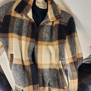 May include: A plaid jacket with a zipper closure. The jacket is made of a thick, woven fabric and has a black, white, and orange plaid pattern. The label on the jacket reads "Hall-American Sportswear, Robert Hall, 38".