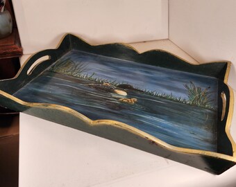May include: A green wooden serving tray with a gold trim and a painted scene of two loons swimming in a lake. The tray has two handles on the sides.