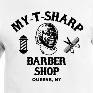 May include: A white t-shirt with a black graphic design that says "My T-Sharp Barber Shop Queens, NY". The graphic also includes a cartoon barber, a barber pole, and a pair of scissors.