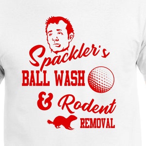 May include: White t-shirt with red text that reads "Spackler's Ball Wash & Rodent Removal". The text is accompanied by a cartoon image of a man and a golf ball.