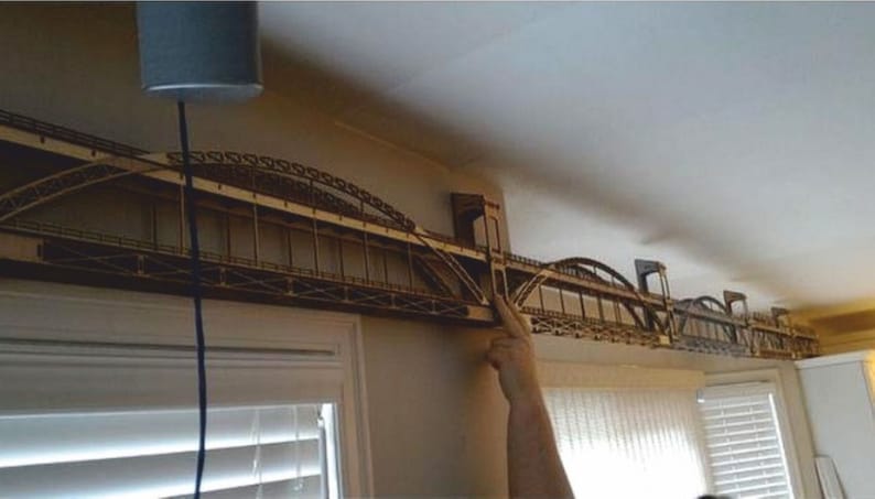 May include: A wooden model of a bridge, with multiple arches, is mounted on a wall. The model is made of light brown wood and appears to be a detailed replica of a real bridge.
