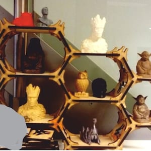 May include: A wooden hexagonal shelf unit with multiple shelves, displaying a variety of small figurines. The figurines include a white Yoda, a brown Yoda, a black and white owl, a black skull, a gray alien, a brown figure with a red hat, and a white figure with a crown.