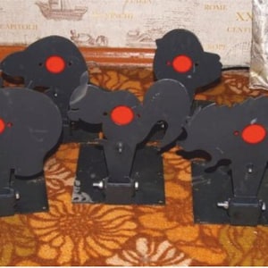 Könnte beinhalten: Ein Satz von zehn schwarzen Silhouettenzielen mit roten Zielscheiben. Die Ziele sind auf schwarzen Sockeln montiert und haben die Form verschiedener Tiere, darunter ein Seepferdchen, ein Kaninchen, ein Löwe und ein Vogel.