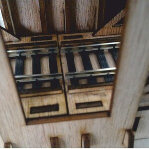 May include: A wooden model train bridge with two sets of tracks. The bridge is made of light brown wood and has a natural wood finish. The tracks are made of black plastic and are laid out in a straight line.