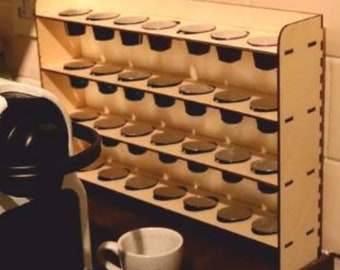 May include: A light-colored wooden coffee pod holder with multiple shelves, each designed to hold individual coffee pods. A white coffee cup and a coffee machine are also visible.