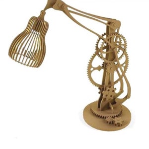 May include: A wooden desk lamp with a geometric shade and a base with intricate gears. The lamp is made of natural wood and has a rustic, industrial look.