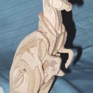 May include: A wooden kangaroo sculpture made of interlocking pieces. The sculpture is light brown and has a jointed tail and legs.