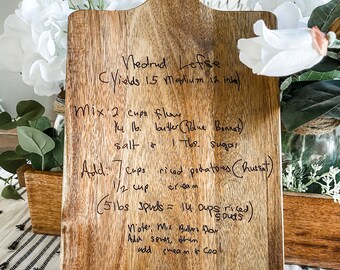 May include: A wooden cutting board with a handwritten recipe for Vedrud Lefse. The recipe includes ingredients like flour, butter, riced potatoes, and cream. It yields 15 medium lefse.