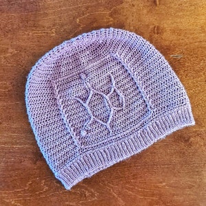 May include: A purple knitted hat with a cable knit pattern.