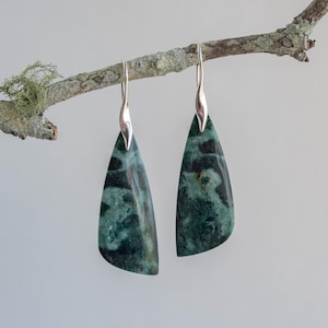 May include: A pair of silver dangle earrings with green and black marbled stone drops. The earrings are hanging from a branch.