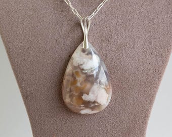 May include: A teardrop-shaped pendant necklace with a silver chain. The pendant is a polished stone with a mix of brown, white, and pink hues. The necklace is displayed on a neutral-colored surface.
