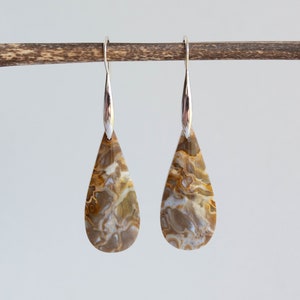 May include: A pair of silver teardrop earrings with brown and white agate stones. The stones have a swirling pattern.