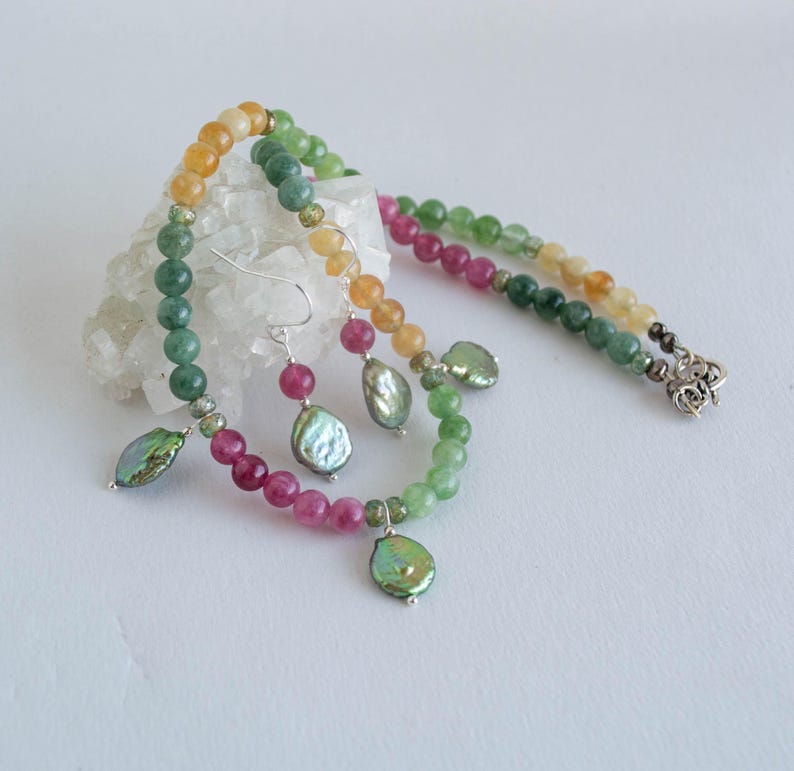 K&ouml;nnte beinhalten: Eine mehrfarbige Perlenkette mit gr&uuml;nen, rosa und gelben Perlen. Die Kette hat einen silbernen Verschluss und mehrere perlmuttartige Anh&auml;nger.