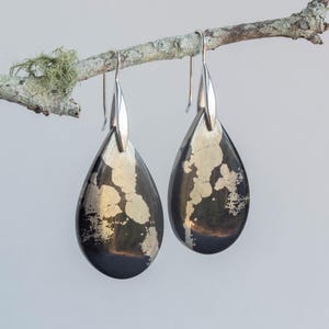 May include: A pair of silver teardrop earrings featuring black and gold pyrite stones. The stones have a natural, irregular pattern.