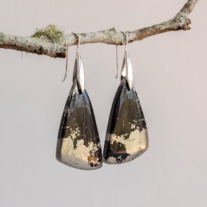 May include: A pair of silver dangle earrings featuring black and gold pyrite stones. The stones are triangular in shape and have a rough, natural texture.