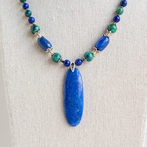 Könnte beinhalten: Eine Halskette aus blauen und grünen Edelsteinen mit einem großen ovalen Anhänger. Die Halskette ist aus silbernen Perlen gefertigt und verfügt über eine Vielzahl von blauen und grünen Steinen.