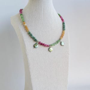 K&ouml;nnte beinhalten: Eine mehrfarbige Perlenkette mit drei schillernden Anh&auml;nger. Die Kette besteht aus gr&uuml;nen, rosa und gelben Perlen.