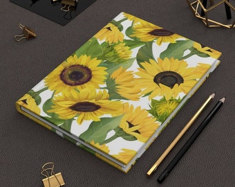May include: A white notebook with a sunflower pattern. The notebook has a yellow cover with a white border. The sunflowers are yellow with green leaves.