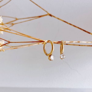 May include: A pair of gold hoop earrings with a small clear stone on each earring.