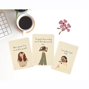 May include: Three affirmation cards with illustrations of women and inspirational messages. The cards are beige with brown text. The first card says "Other's opinions of me do not define my worth." The second card says "I'm going to focus on doing more of what makes me feel alive." The third card says "I am worthy of good things."
