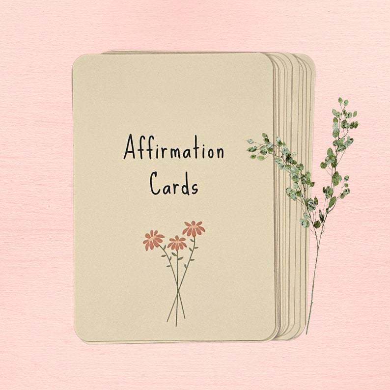 May include: A stack of beige affirmation cards with the text "Affirmation Cards" and a simple illustration of three pink flowers.