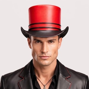 May include: A top hat featuring a vibrant red crown and a contrasting black brim. The hat is accented with two thin black leather bands wrapped around the base of the crown, creating a distinct horizontal line detail against the smooth red surface.