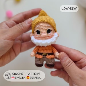 Könnte beinhalten: Eine kleine gehäkelte Zwergenpuppe mit senfgelber Zipfelmütze, runder Drahtbrille und weißem Bart. Die Figur trägt ein orangefarbenes Oberteil, einen braunen Gürtel mit gelber Schnalle und eine braune Hose. Der Text lautet LOW-SEW und CROCHET PATTERN.