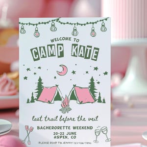May include: A white card with green and pink illustrations of a campfire and tents. The text on the card reads "Welcome to Camp Kate, last trail before the veil, Bachelorette Weekend, 20-22 June, Aspen, CO, Please RSVP to Jenny 123-456-7890".
