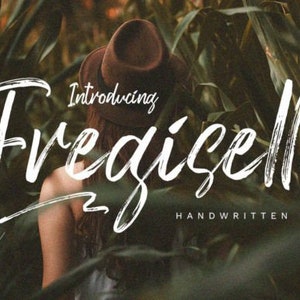 以下が含まれることがあります： ブラシストローク効果のある白いスクリプトフォント「Fredigzelle」を紹介します。緑の葉のぼやけた背景に表示されます。