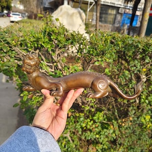 May include: A bronze sculpture of a mythical creature, possibly a dragon or a lion, with a long tail and a fierce expression. The sculpture is detailed and intricate, with scales and fur visible.