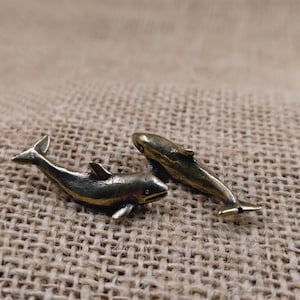 May include: Two small bronze dolphin figurines on a brown hessian background.