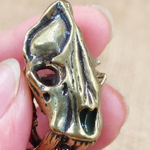 Op de afbeelding: Een ring van goudkleurig metaal met een gedetailleerd schedelontwerp. De schedel heeft een getextureerd oppervlak en een klein gaatje voor het oog. De ring is een statement piece met een gotische esthetiek.