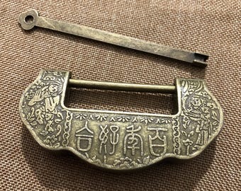 May include: An antique bronze-colored lock with a matching key. The lock has intricate carvings and Chinese characters. The key is a long, slender bar with a circular hole on one end. The lock is rectangular with a curved top and bottom.