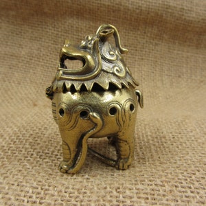 May include: A detailed brass incense burner shaped like a mythical lion-like creature. The burner has intricate details, including a stylized mane, open mouth, and decorative perforations. The overall color is a warm, aged brass tone, suggesting an antique or vintage aesthetic.