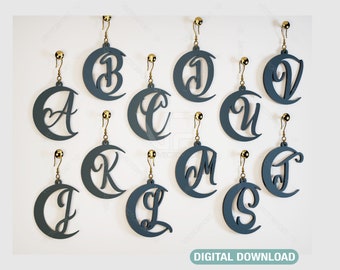 May include: A set of 12 pairs of earrings featuring a crescent moon design with a letter cut out in the center. The earrings are made of a dark blue material and have gold-colored hooks.