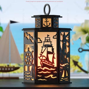 May include: Black nautical lantern with cut-out designs of a ship, anchor, lighthouse, and steering wheel. The lantern has a handle and is illuminated from within, creating a warm glow. A sailboat model is in the background.