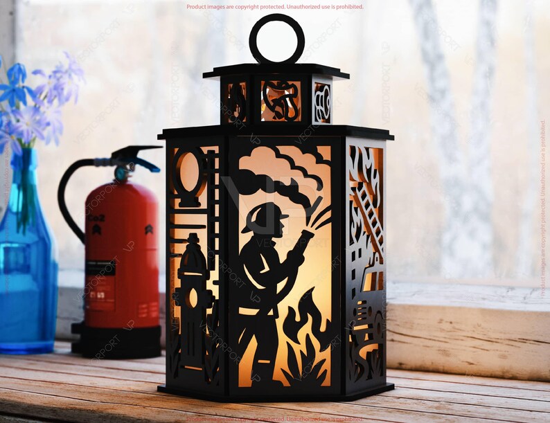 May include: Black decorative lantern with a firefighter silhouette design. The lantern features cut-out details of a firefighter, fire, ladder, and fire hydrant. The lantern has a handle and is placed on a wooden surface.
