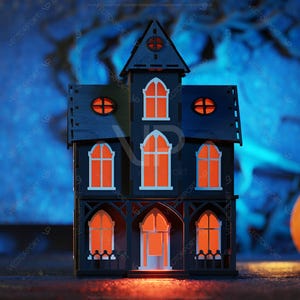 May include: A black wooden haunted house with orange glowing windows, sitting on a dark surface in front of a blue and white blurred background.