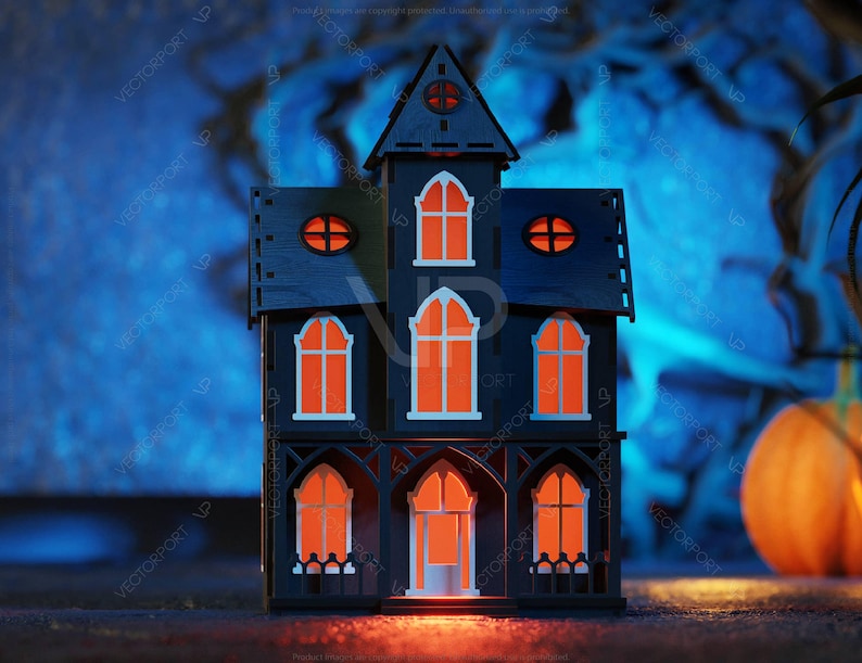 May include: A black wooden haunted house with orange glowing windows, sitting on a dark surface in front of a blue and white blurred background.