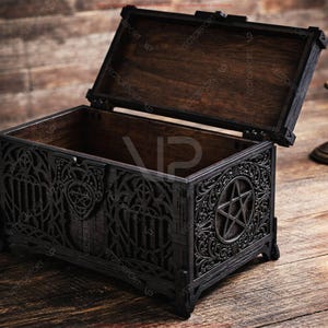 May include: An open, black wooden chest with intricate gothic carvings and a pentagram design on the front. The interior is dark brown. A lit candle in a brass holder sits to the right, on a wooden surface.