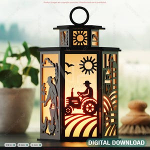 Könnte beinhalten: Eine schwarze dekorative Laterne mit ausgeschnittenen Silhouetten von Bauernhofszenen. Die Laterne zeigt einen Bauern, einen Traktor, die Sonne und Vögel. Die Laterne wird von innen beleuchtet und erzeugt einen warmen Schein. Der Text "DIGITAL DOWNLOAD" ist sichtbar.